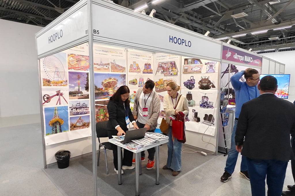 Представительница Hooplo Rides обсуждает с клиентами проекты аттракционов и возможности сотрудничества за ноутбуком и печатными каталогами на стенде, RAAPA EXPO Осень 2026 Москва.