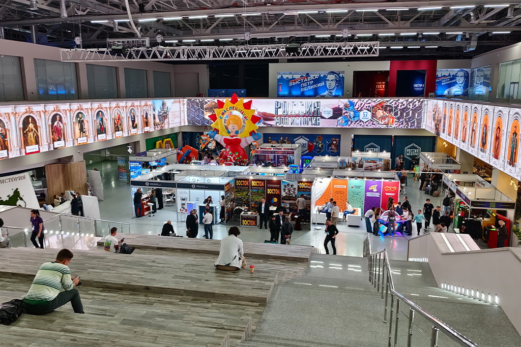 Общий вид выставочного зала RAAPA EXPO Осень 2026 в Москве, посетители проходят между стендами аттракционов и развлекательного оборудования на отраслевой выставке индустрии развлечений в России.
